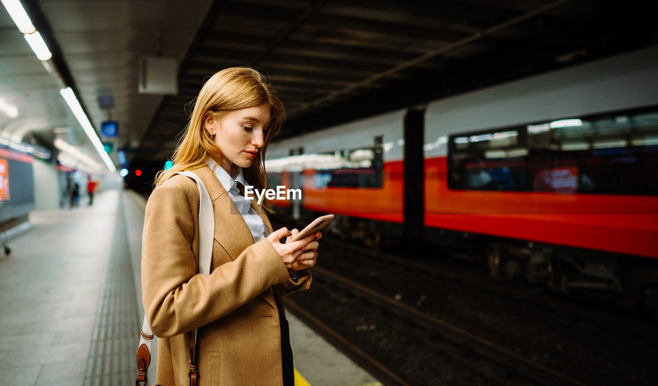 Young long-haired woman messaging phone while standing on the subway