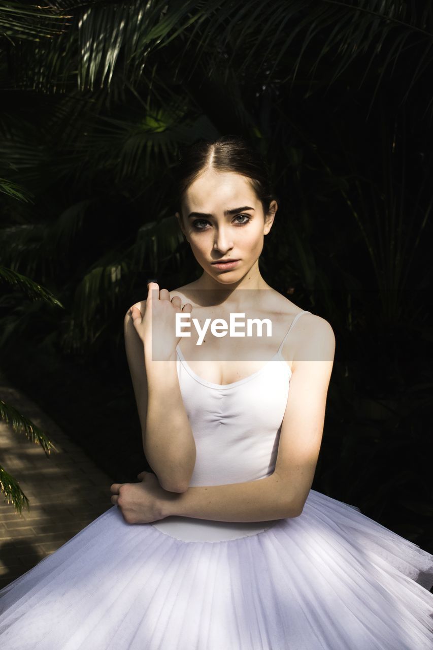 Portrait of ballet dancer sitting against plants