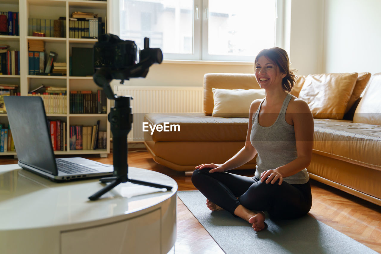 Smiling woman filming while sitting on mat at home