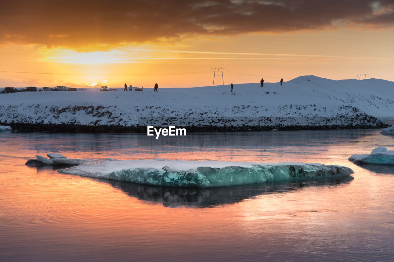 Iceberg floating in sea against sky during sunset