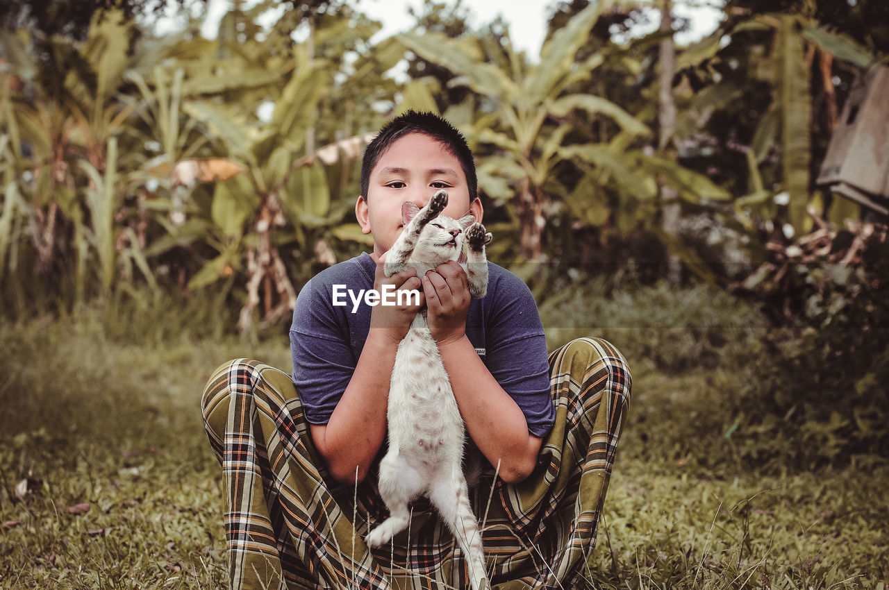 Portrait of teenage boy with cat on field