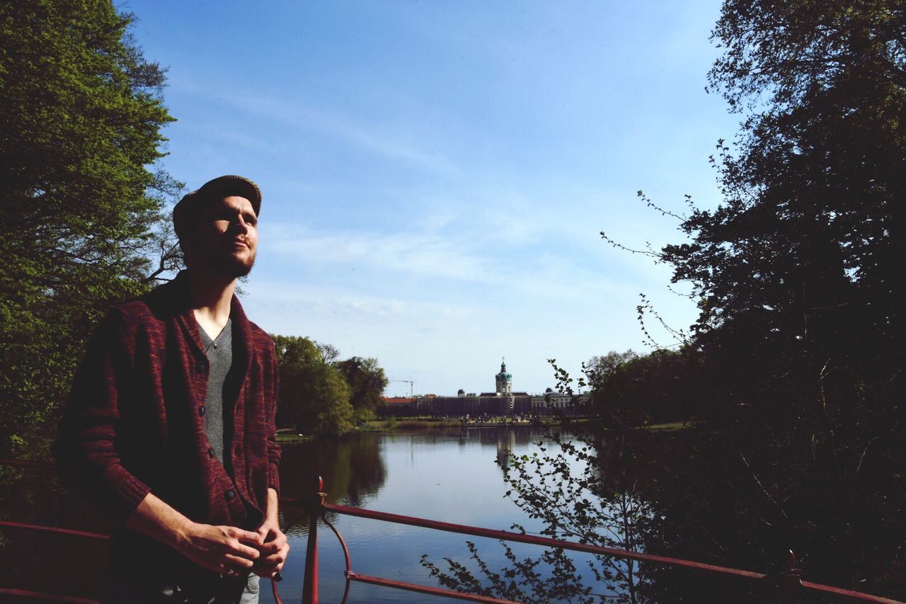 Young man standing by railing against sky