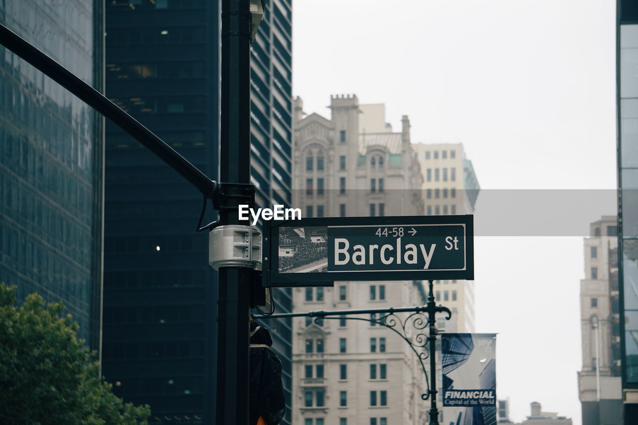 Road sign by buildings against sky in city