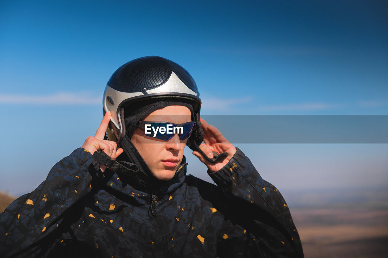 A young male paraglider in sunglasses fastens his helmet on a sunny day. preparing for paragliding