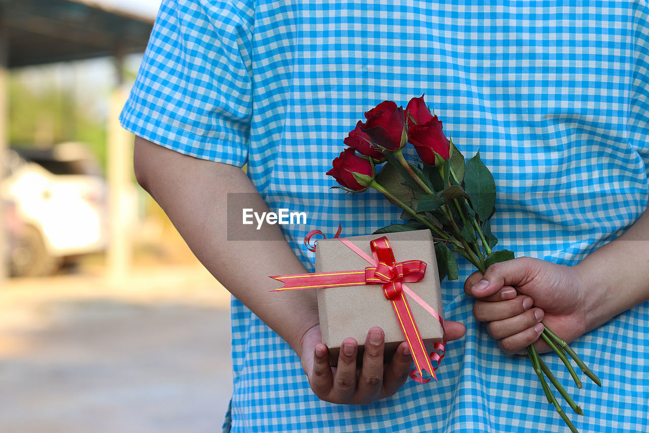 Midsection of man holding gift box and roses