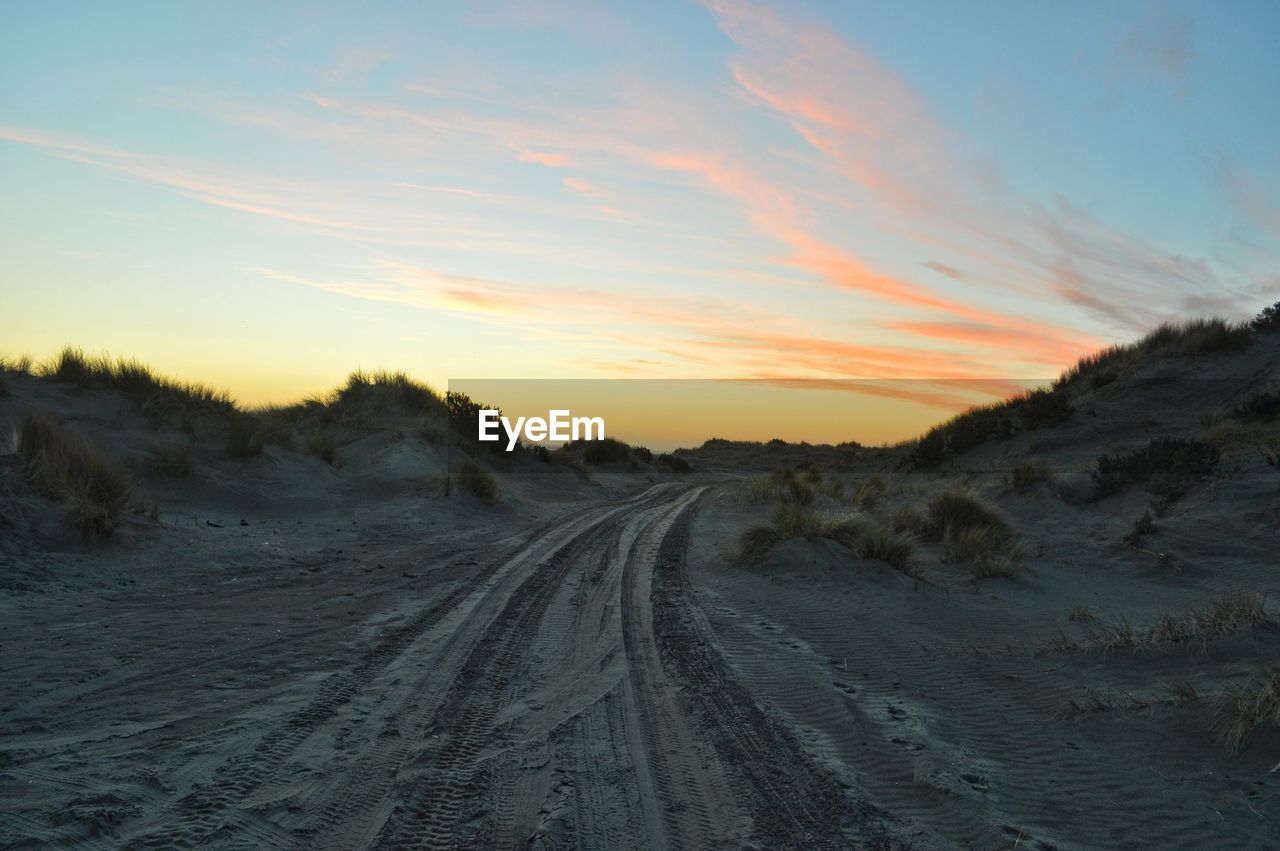 TIRE TRACK ON ROAD AGAINST SKY DURING SUNSET