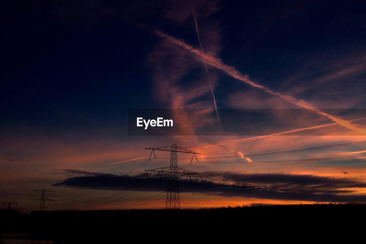 Electricity pylons on silhouette field against sky during sunset