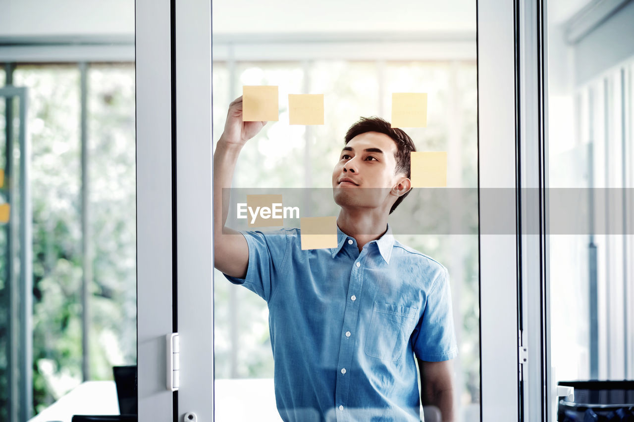 Businessman sticking adhesive note on window at office