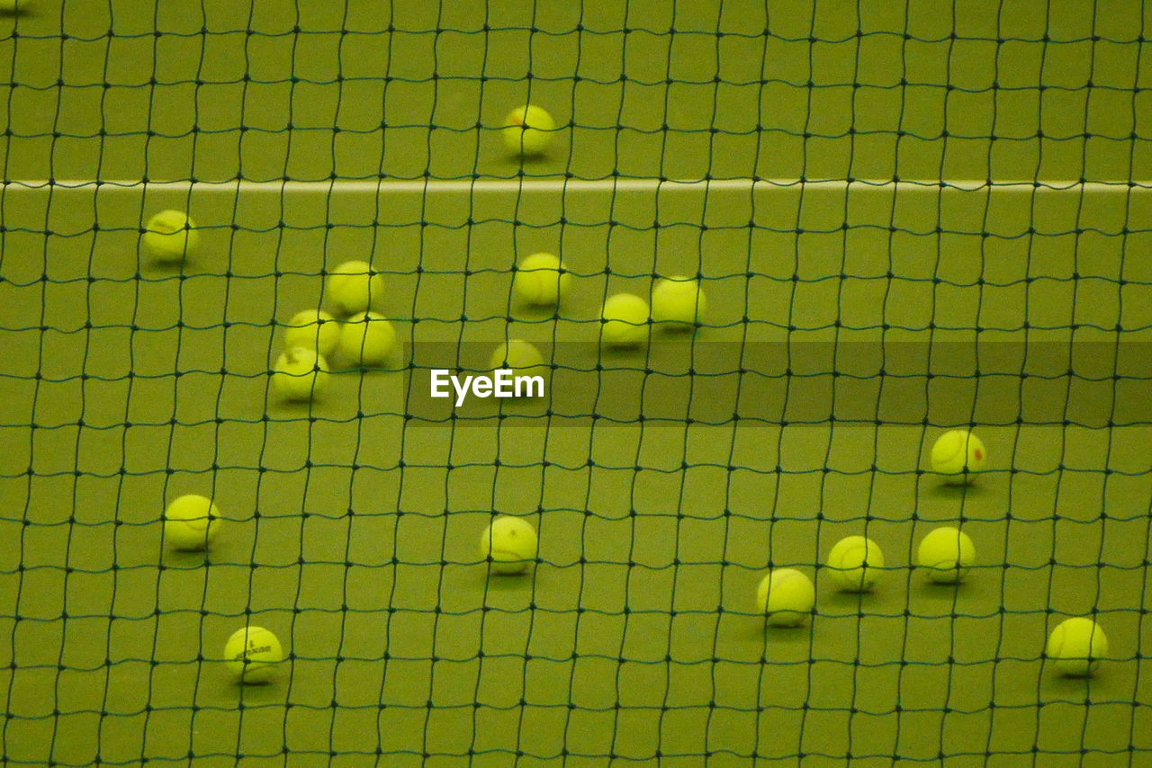 High angle view of tennis balls on court seen through net