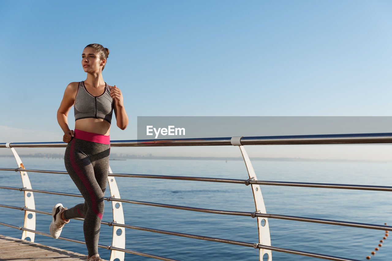 Full length of woman running by railing against sea