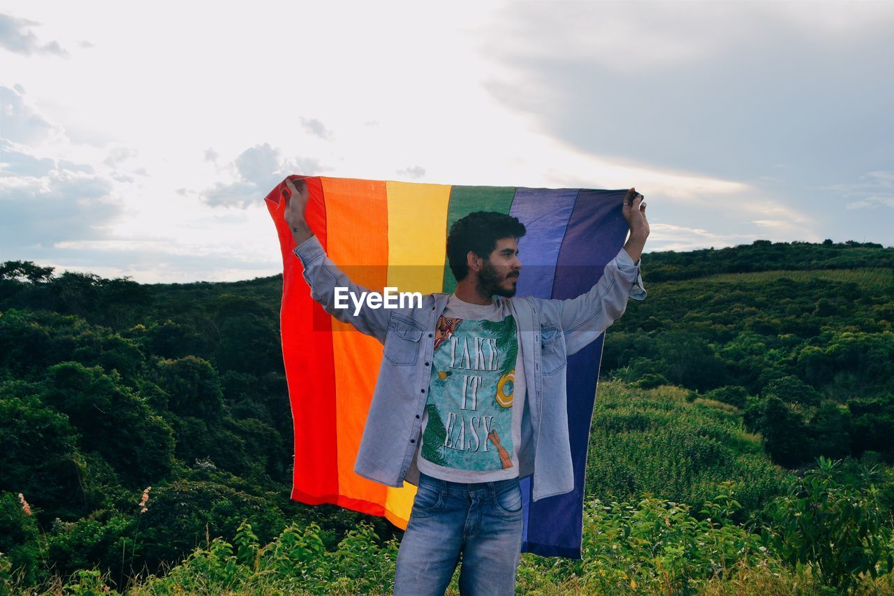 Man holding rainbow flag against sky