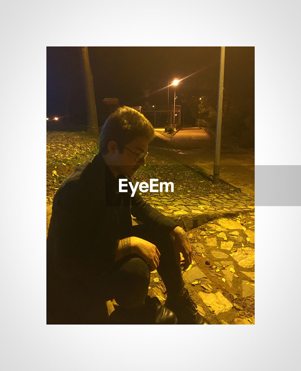 YOUNG MAN LOOKING AT ILLUMINATED WHILE SITTING AT NIGHT DURING FESTIVAL