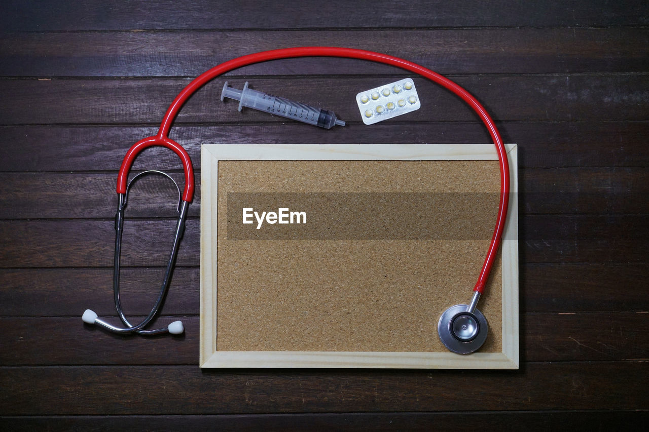 High angle view of picture frame with syringe and stethoscope on wooden table