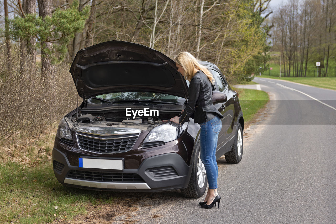 Full length of fashionable young woman standing by breakdown car on roadside