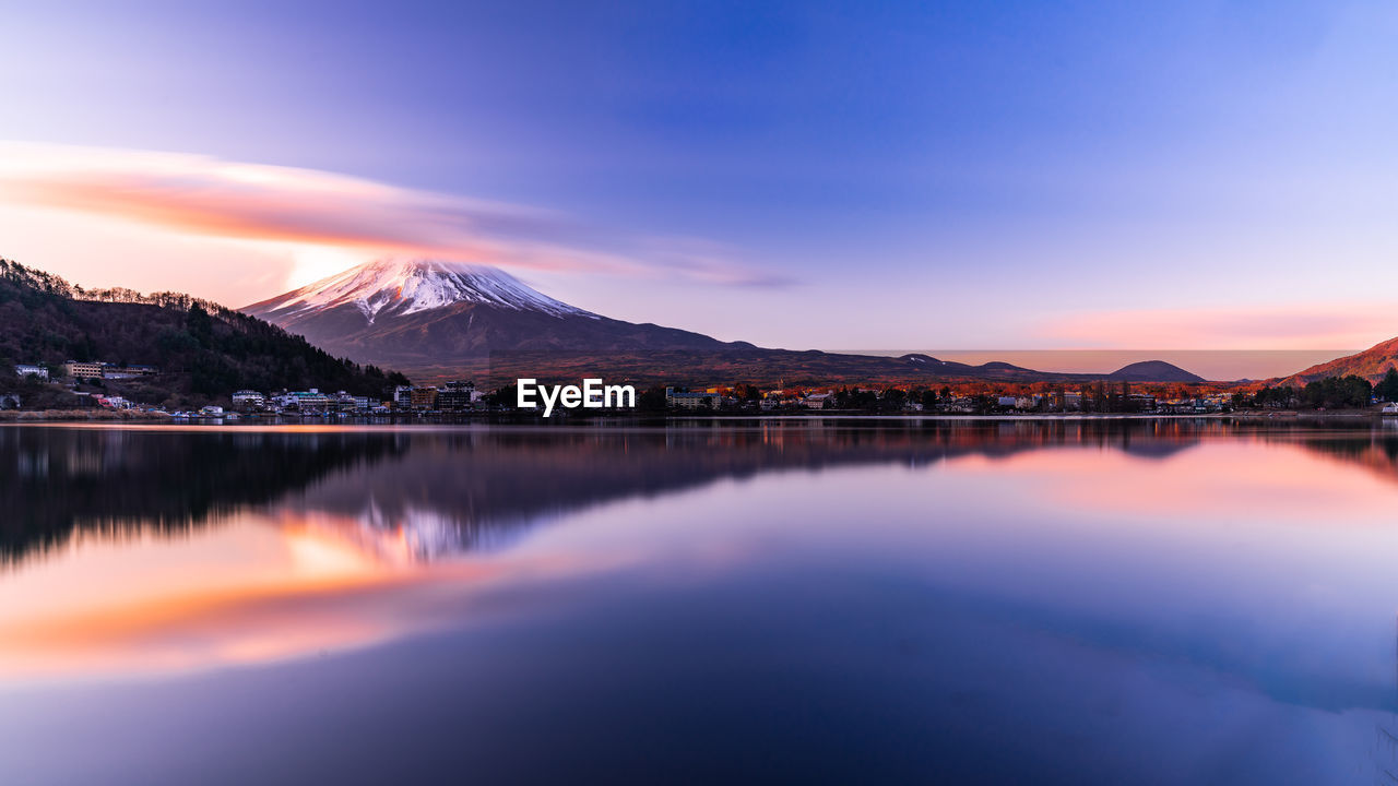 Scenic view of lake by snowcapped mountains against sky during sunset