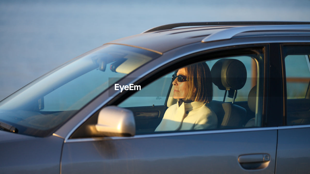 Senior elegant lady enjoying sunset from a car at the coast