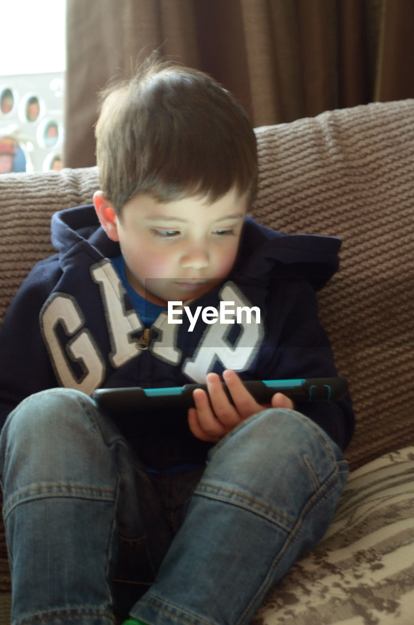 Close-up of boy using digital tablet on sofa at home