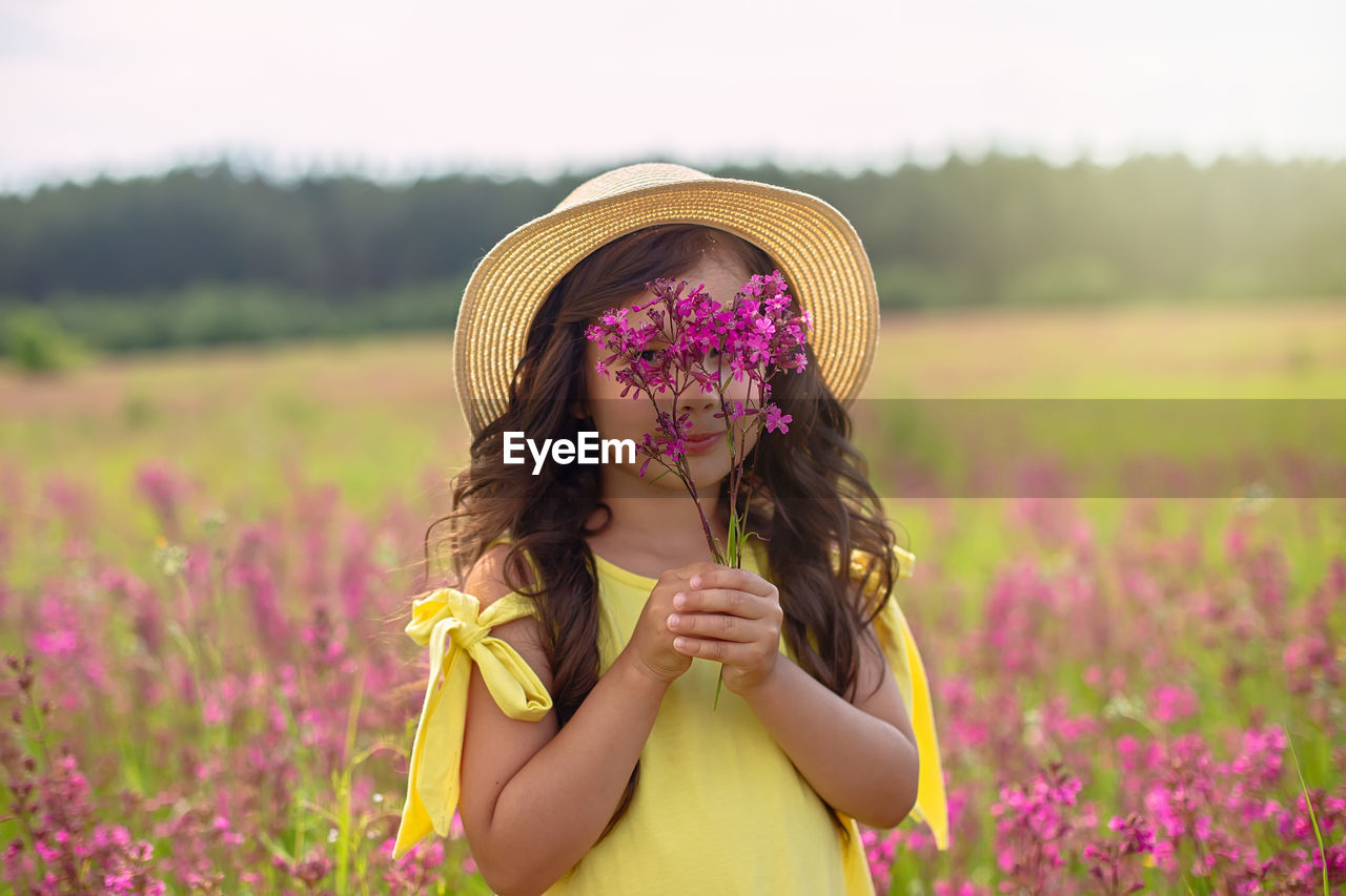 A beautiful playful little girl in a straw hat, holds a bouquet of burgundy viscaria flowers