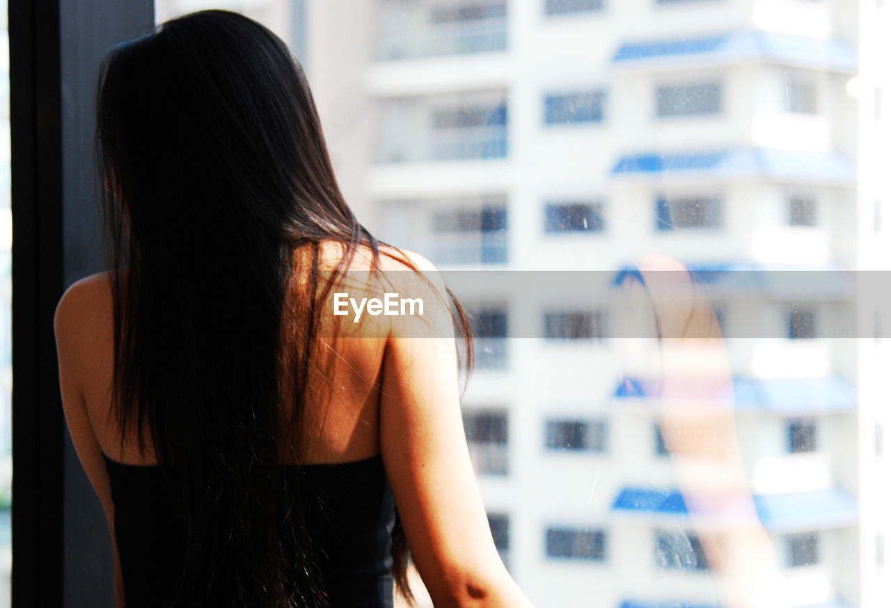 Rear view of woman standing by glass window