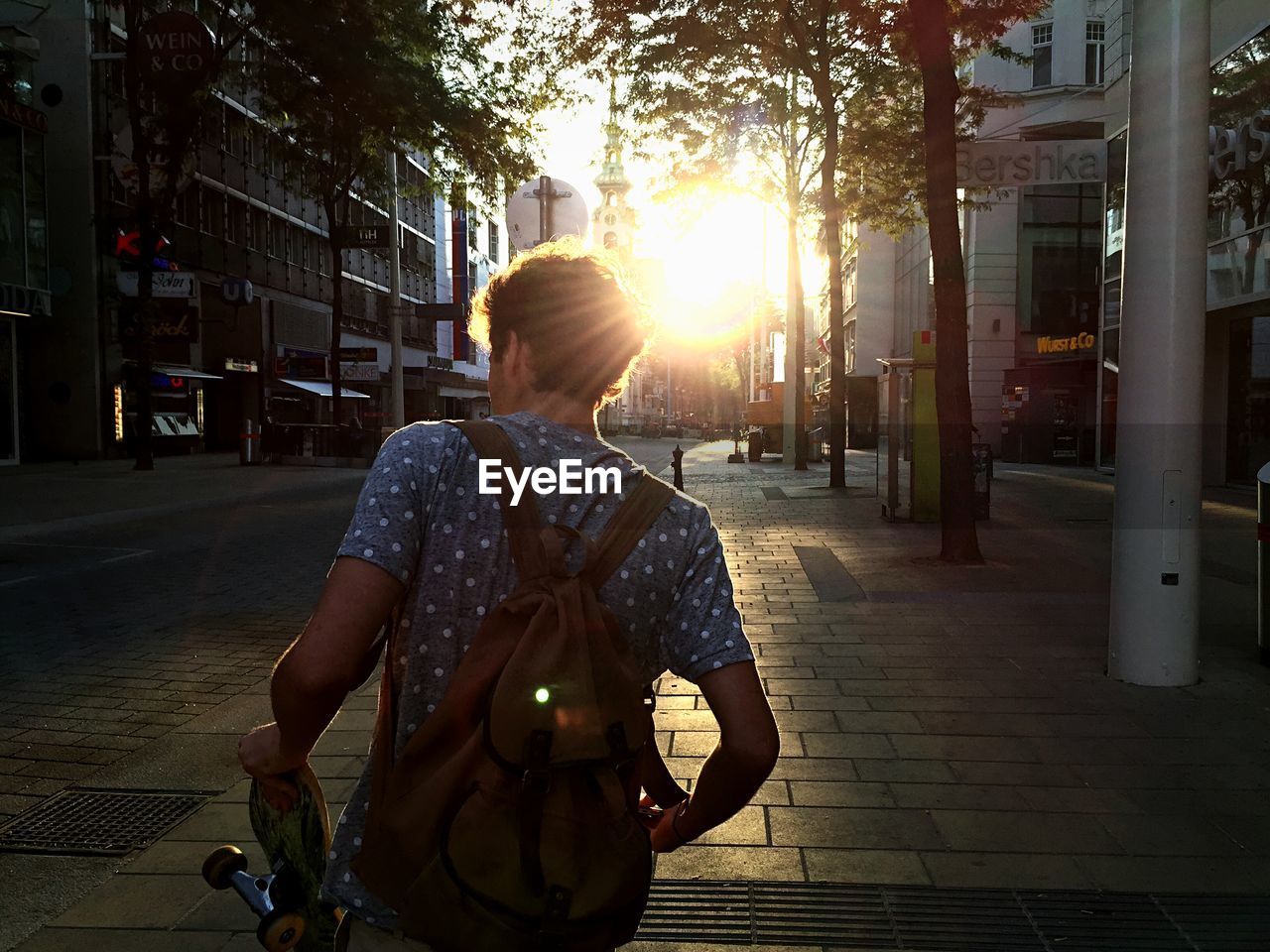 Rear view of man walking in sidewalk in city at morning