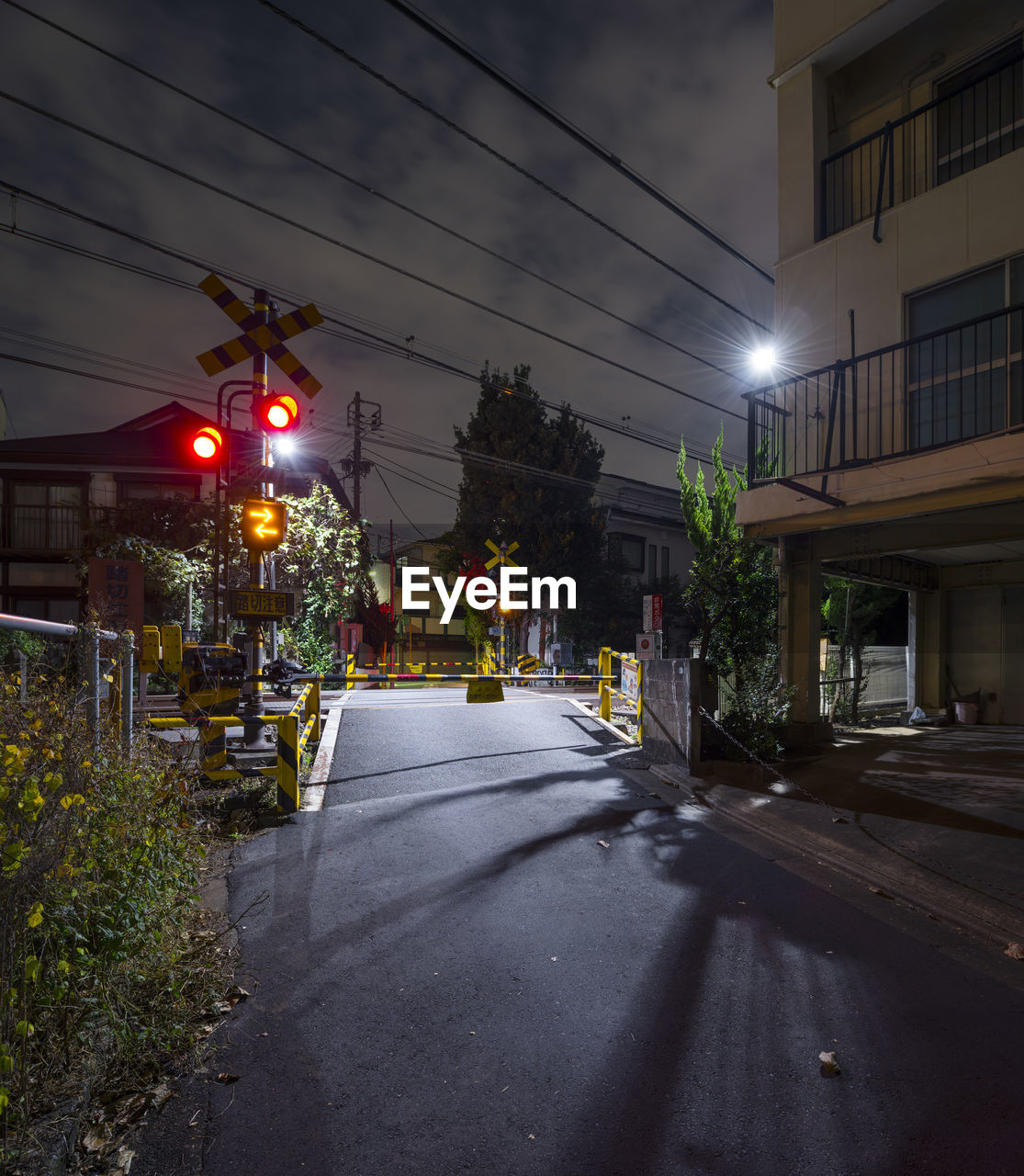 Empty road by illuminated railroad crossing signal against sky at night