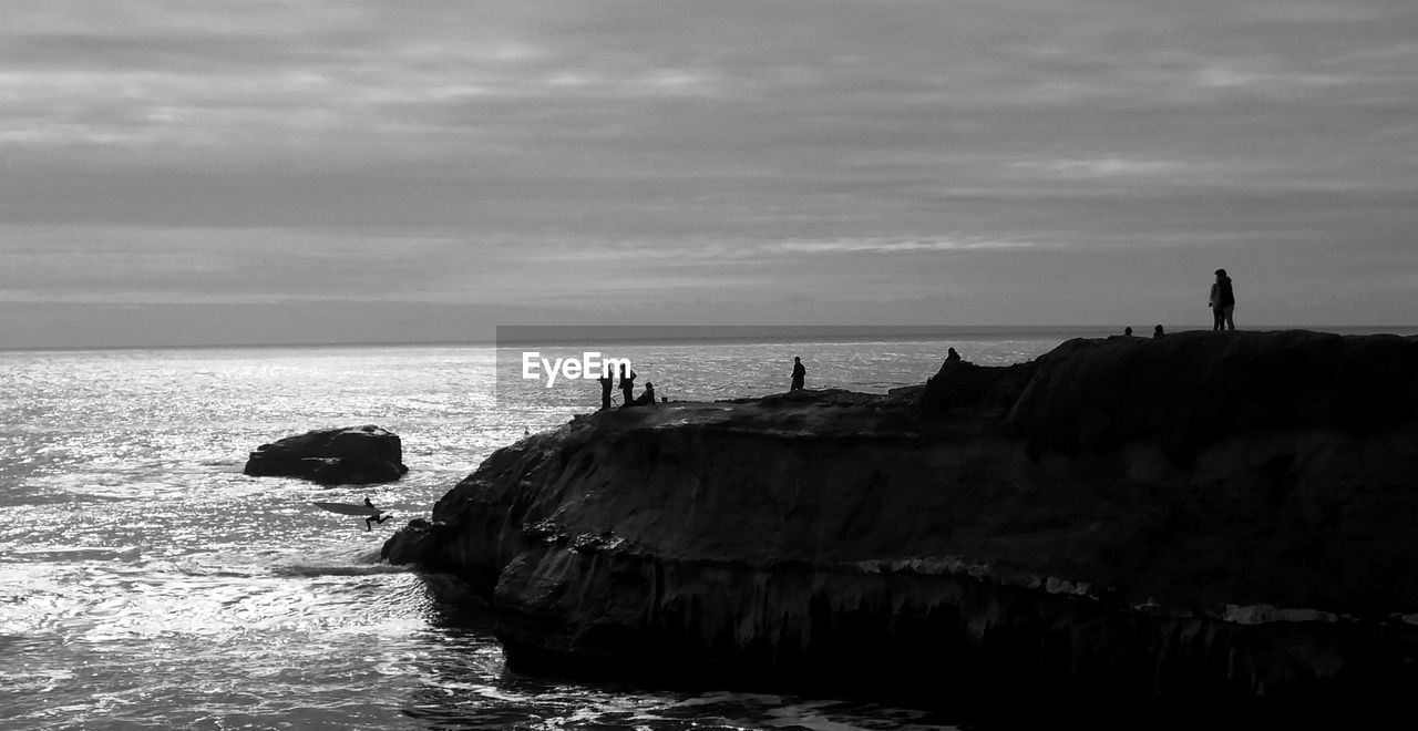 People on rock formation in sea against sky