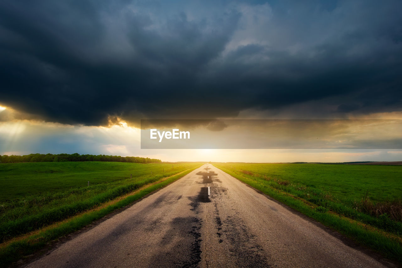 Road amidst field against sky during sunset