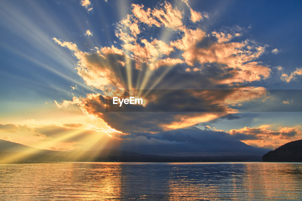 Sunlight streaming through clouds over lake yamanaka during sunset