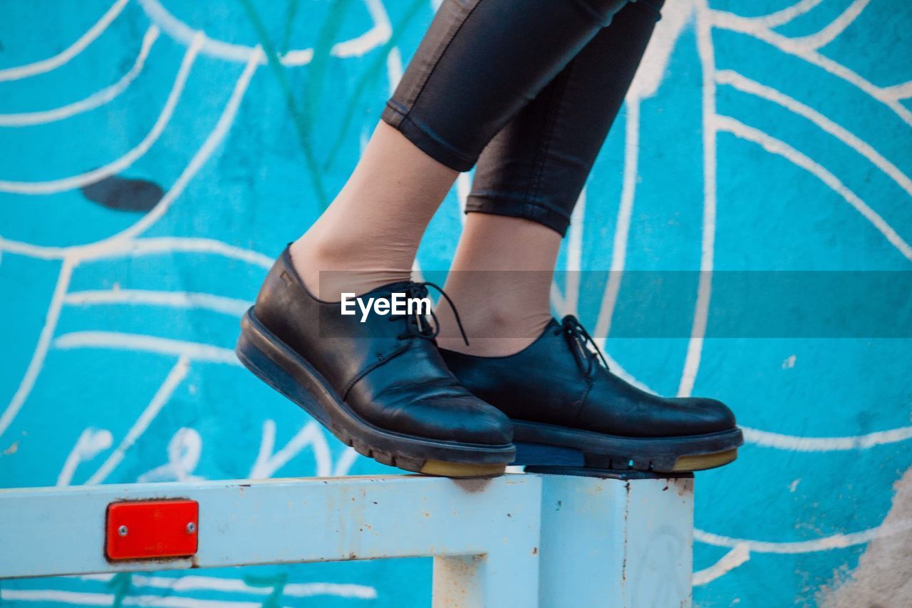 Low section of woman standing on metal against wall