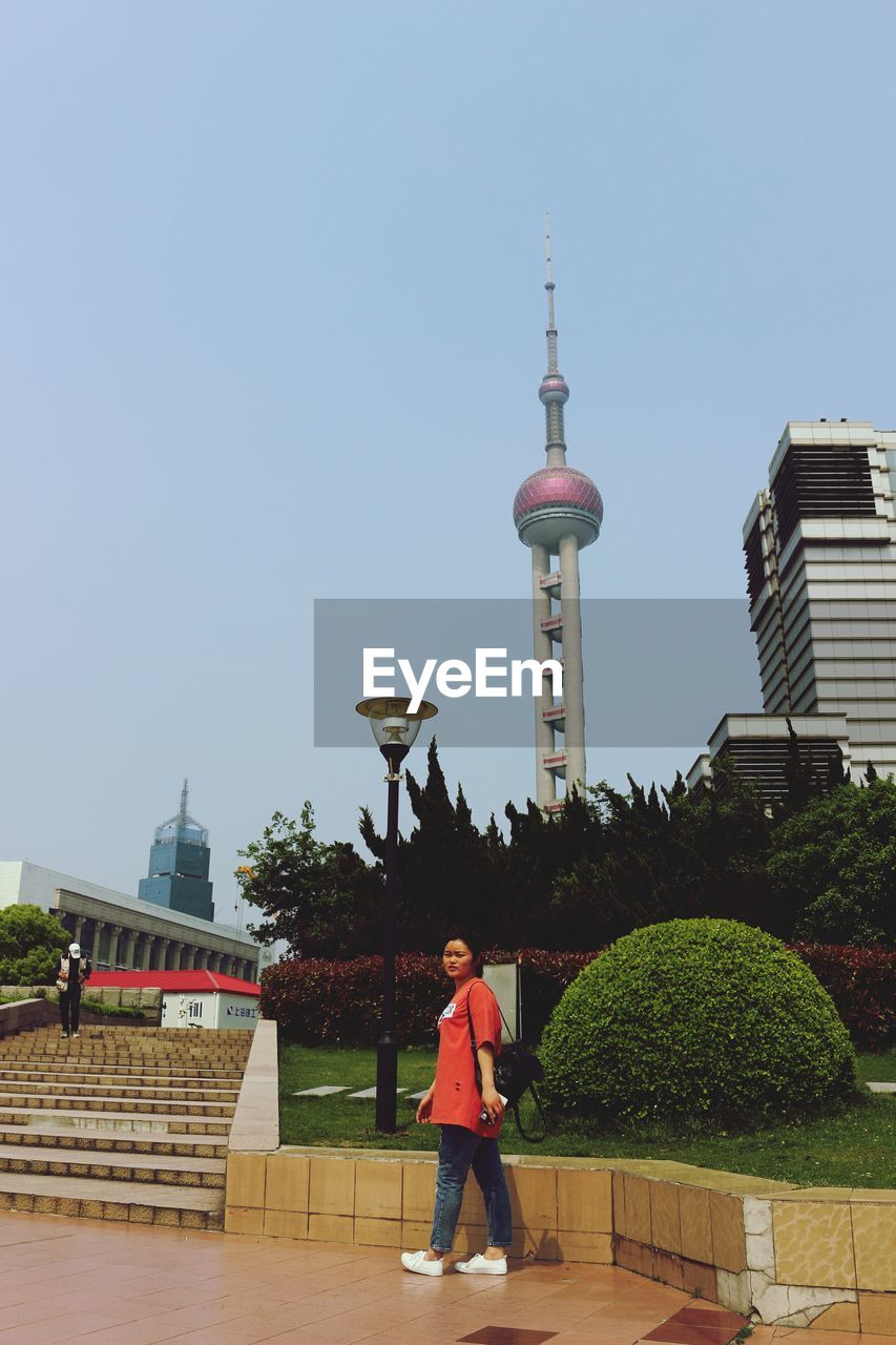REAR VIEW OF MAN STANDING AGAINST BUILDINGS