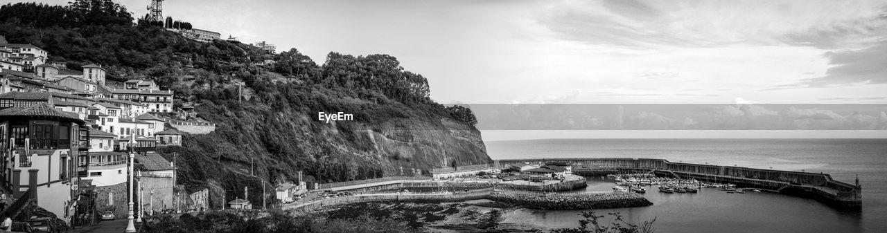 Panoramic view of harbor on sea by mountain against sky