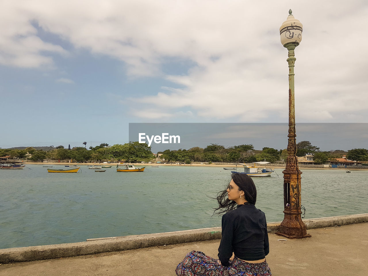 REAR VIEW OF WOMAN SITTING ON RIVERBANK AGAINST SKY