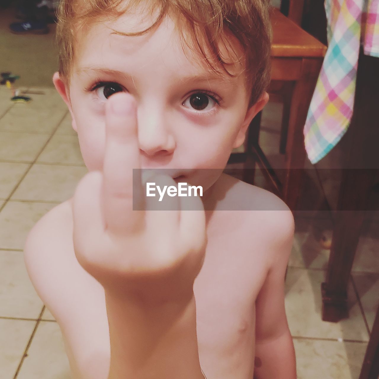 Portrait of shirtless boy showing obscene gesture at home