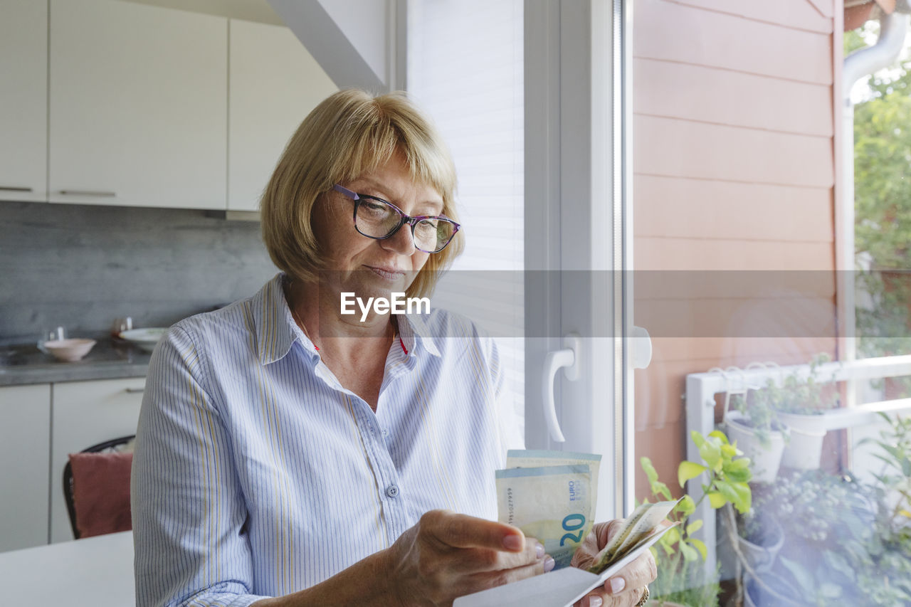 Senior woman with eyeglasses counting paper currency at home