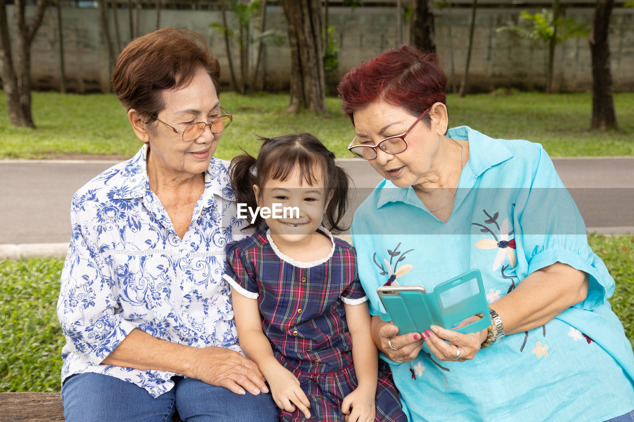 Family shot of two grandmothers and their adorable granddaughter posing happily in the park outdoor 