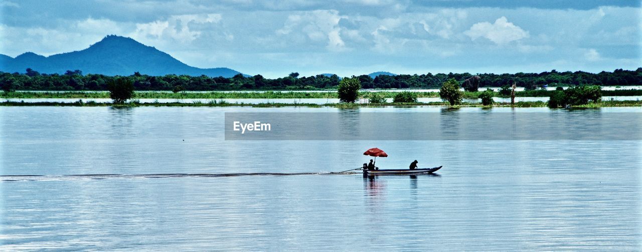 Men in boat on lake against sky