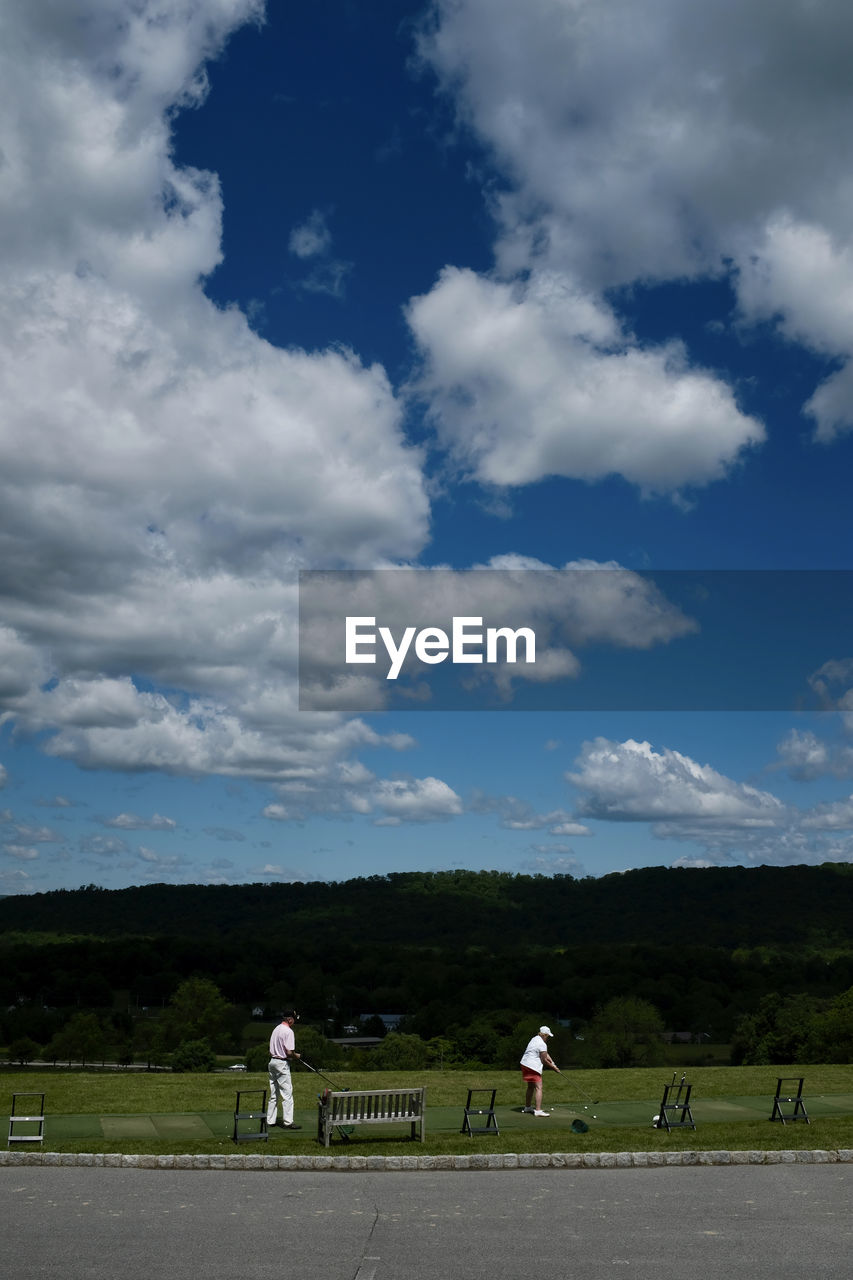 PEOPLE STANDING ON GREEN LANDSCAPE AGAINST SKY