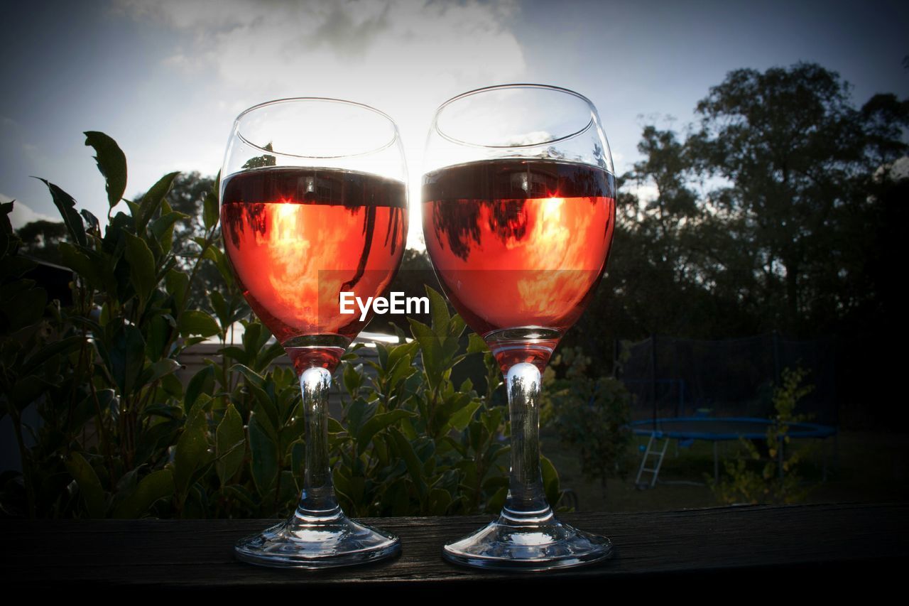 Close-up of rose wine glasses on table in back yard against sky