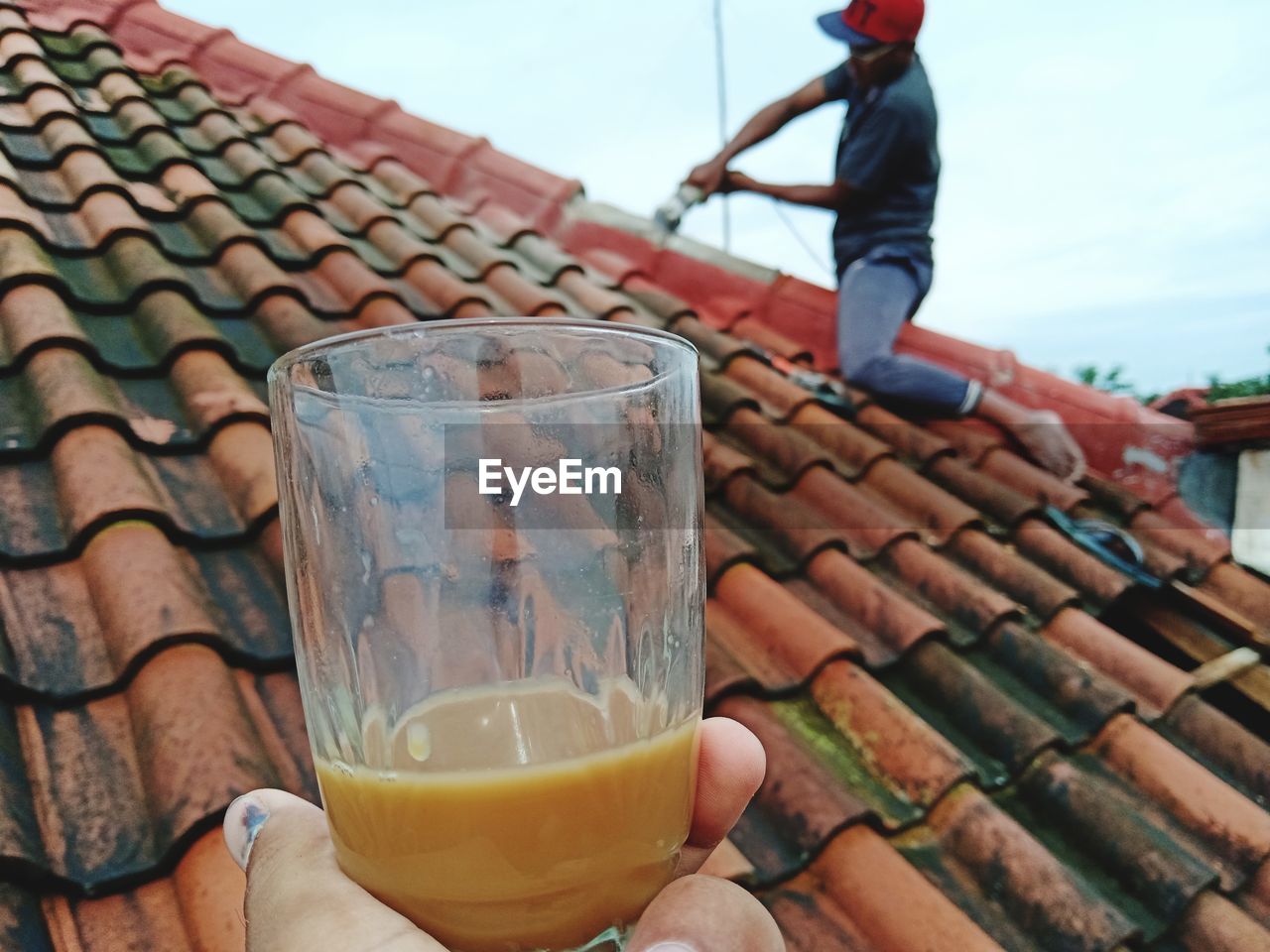 Cropped hand holding tea with man working on roof in background