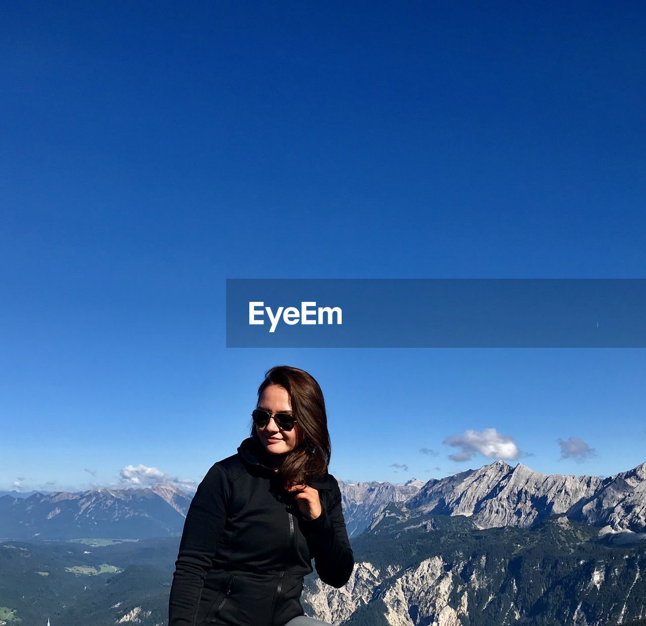 Portrait of woman standing on snowcapped mountain against blue sky