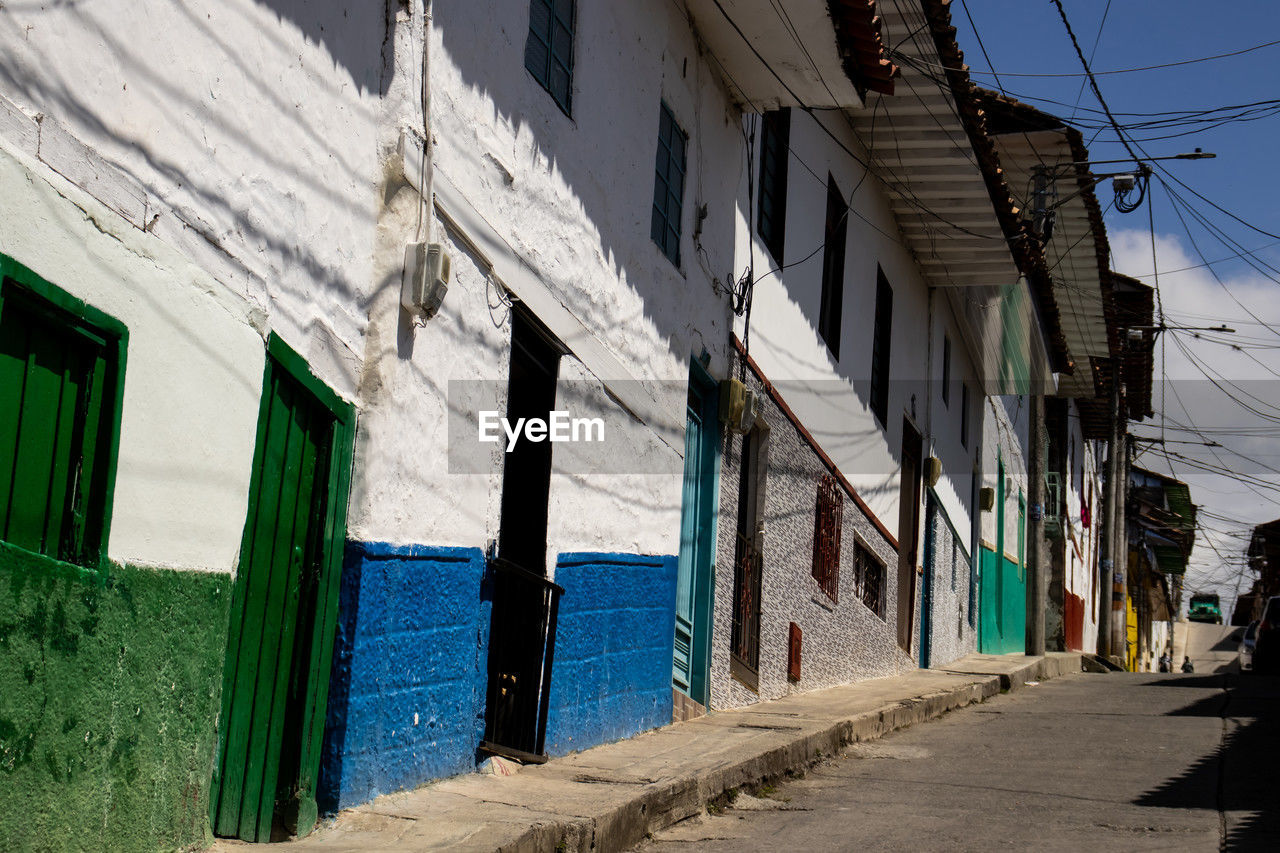 urban area, road, architecture, street, building exterior, built structure, neighbourhood, alley, infrastructure, blue, building, town, city, day, nature, wall, house, residential district, no people, sky, sunlight, outdoors, shadow, wall - building feature, lane