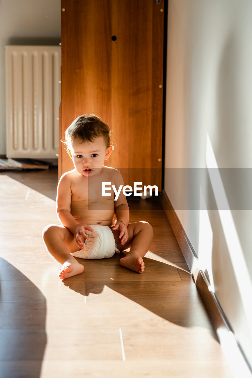 Cute baby girl sitting on wooden floor at home