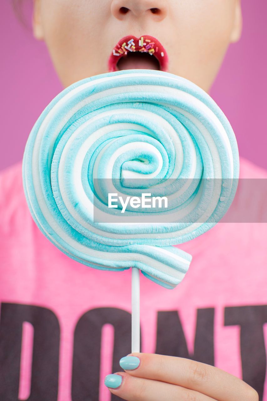 Close-up of woman holding blue lollipop standing against pink background