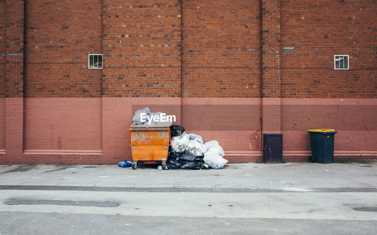 Garbage bin on sidewalk against brick wall