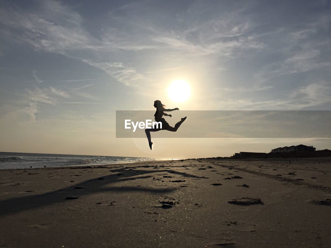 Woman jumping at beach against sky on sunny day