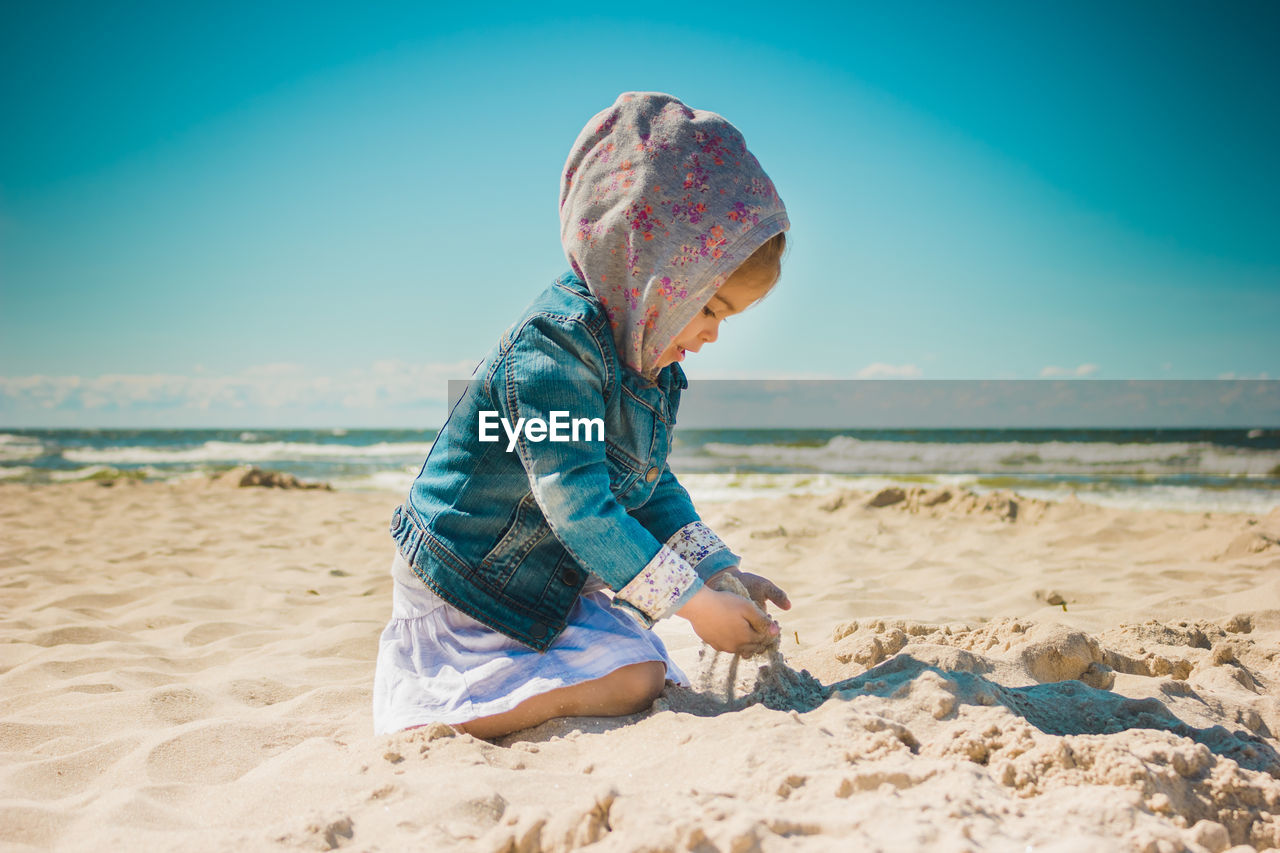 Girl playing with sand while kneeling at beach