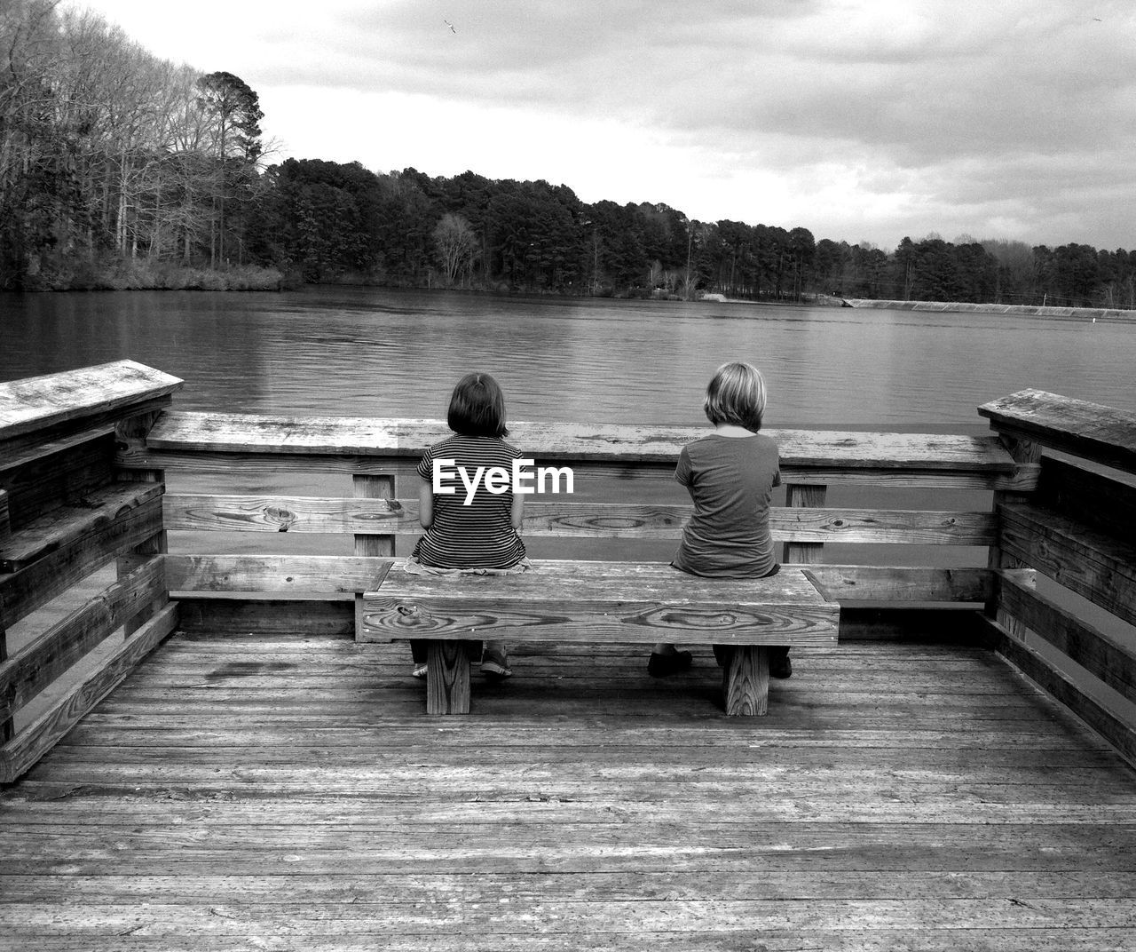 Rear view of siblings sitting on pier in front of lake