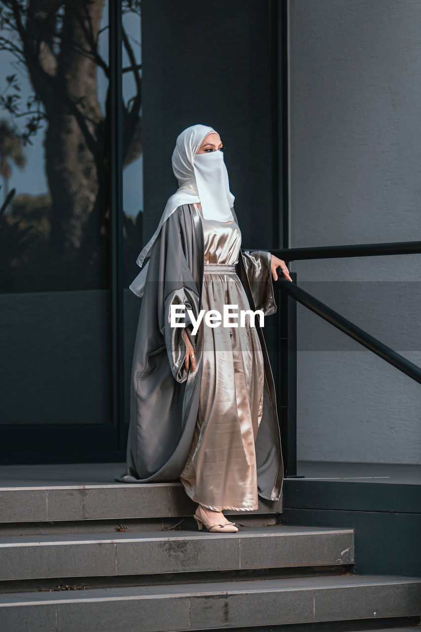 Full length image of veiled woman with white niqab walking down the stairs