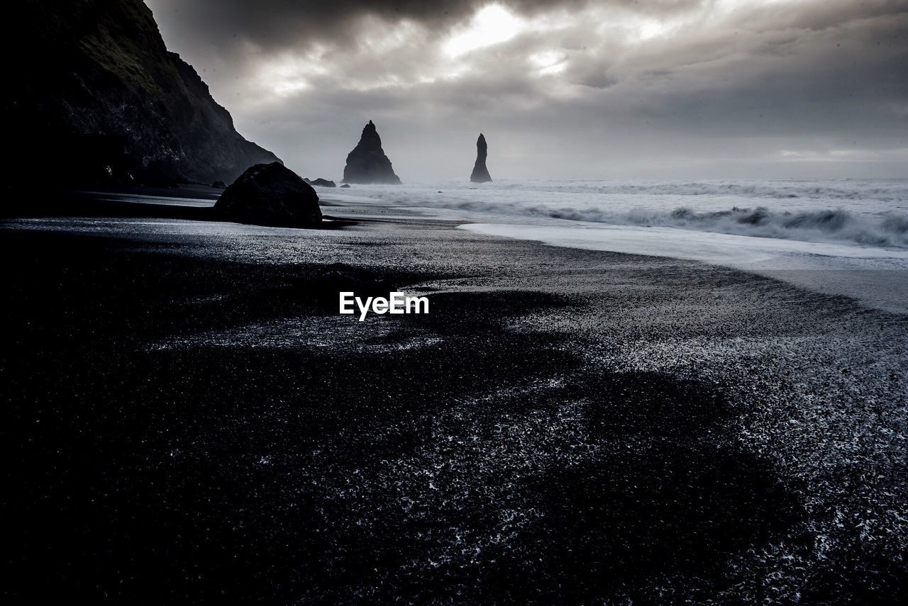 View of calm beach against cloudy sky