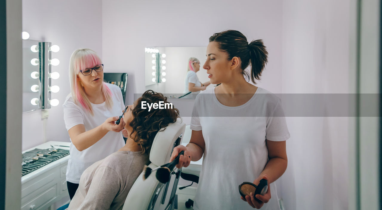 Beauticians applying make-up of woman face at spa